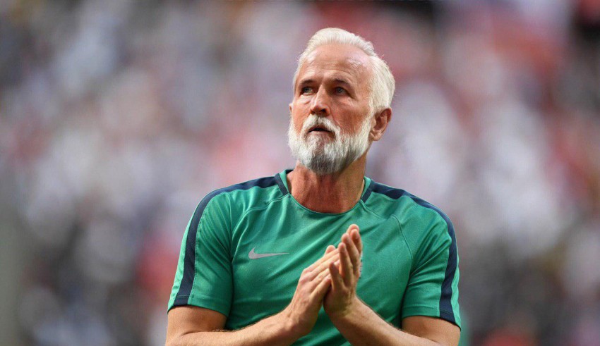 An older man with a beard applauding on the field.