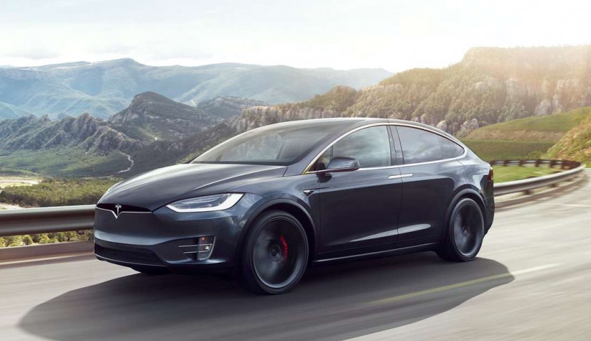 The tesla model x is driving down a mountain road.