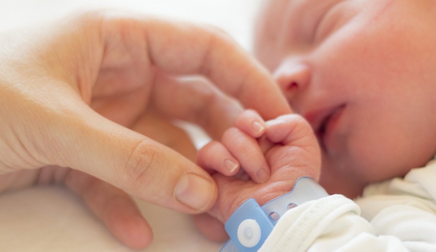 A person's hand is holding a baby's hand.