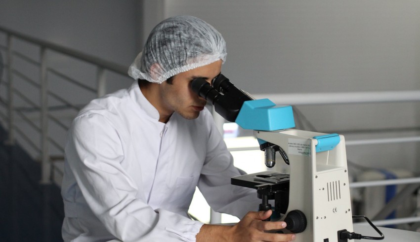 A man in a lab looking through a microscope.