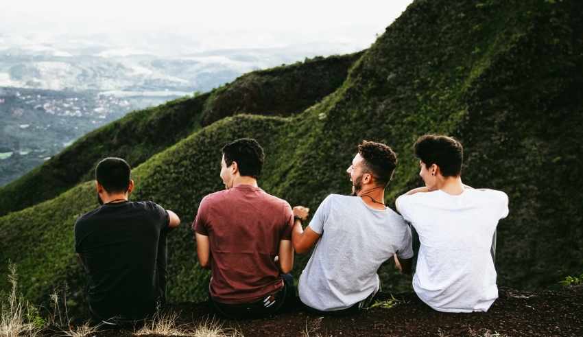 Four young men sitting on top of a hill overlooking a valley.