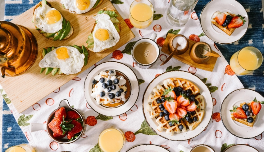 Waffles, eggs, fruit and juice on a tablecloth.