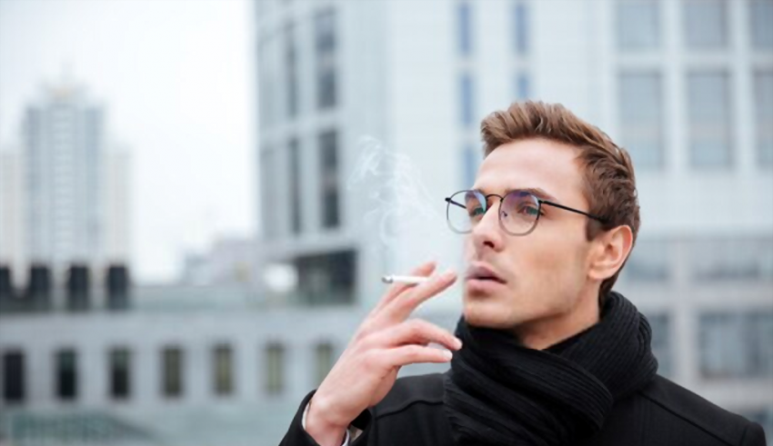 A man in glasses smoking a cigarette in a city.