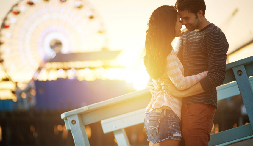 A couple embracing in front of a ferris wheel at sunset.