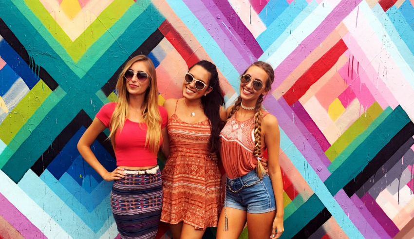Three women posing in front of a colorful wall.