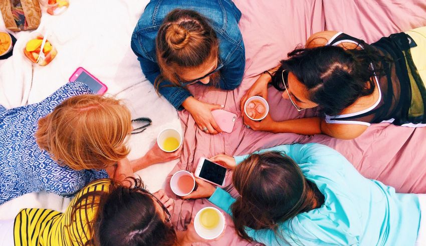 A group of women sitting in a circle on a pink blanket.