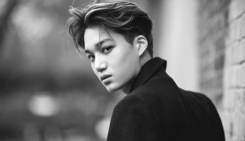 A black and white photo of a young man leaning against a brick wall.