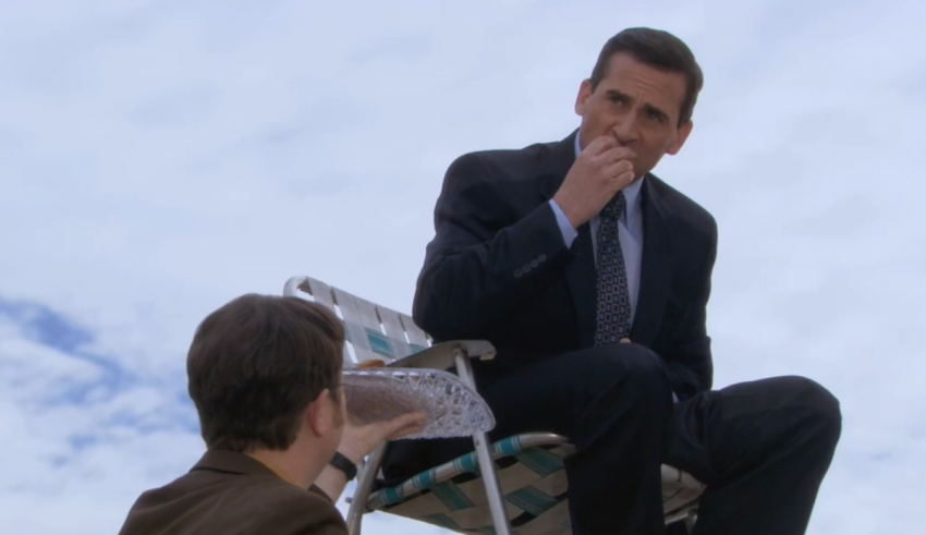 A man in a suit sits on a chair next to a man in a suit.