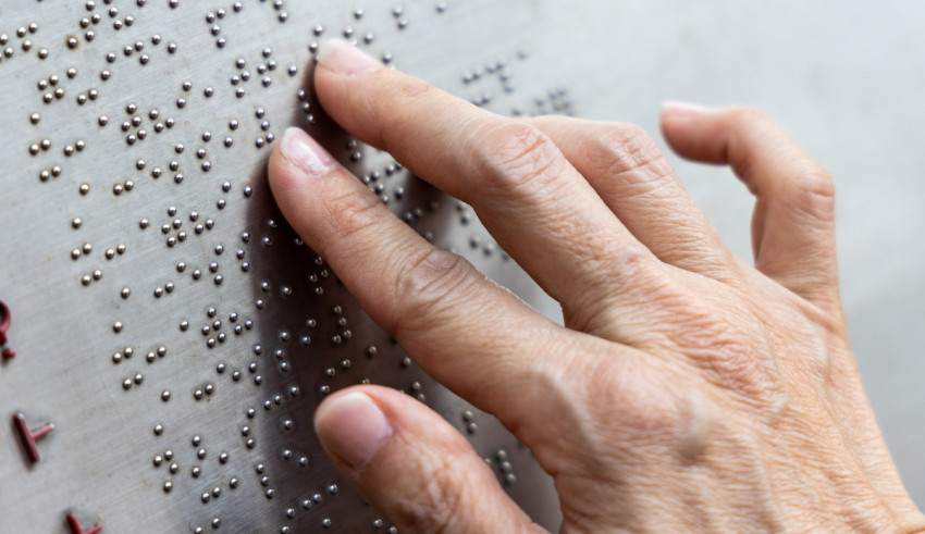 A woman's hand is touching a metal wall with braille.