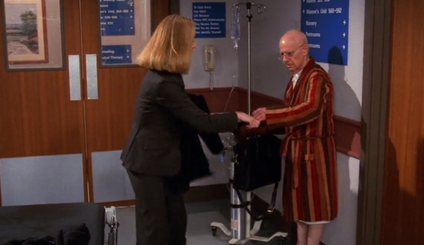 A man in a robe is shaking hands with a man in a hospital bed.