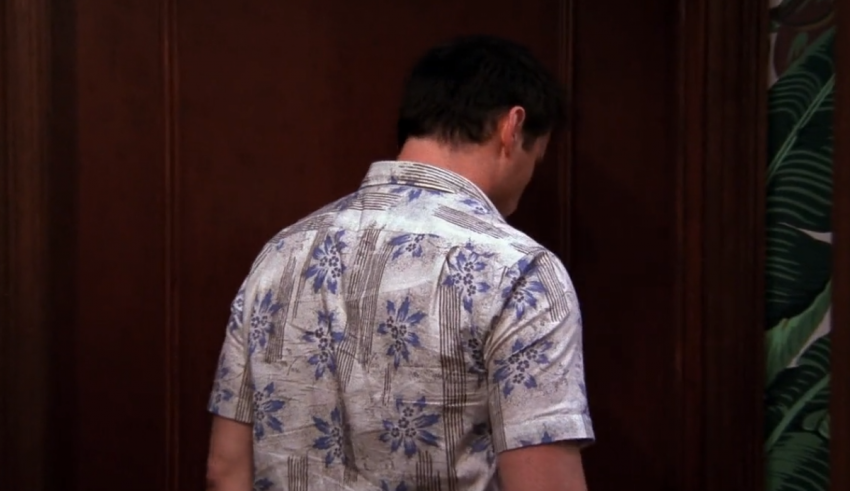 A man in a hawaiian shirt is standing in front of a door.