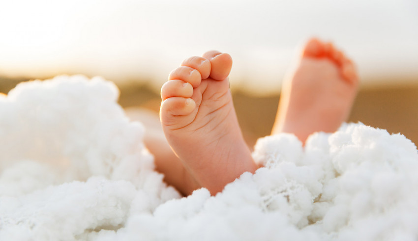 A baby's feet are laying on top of a white blanket.