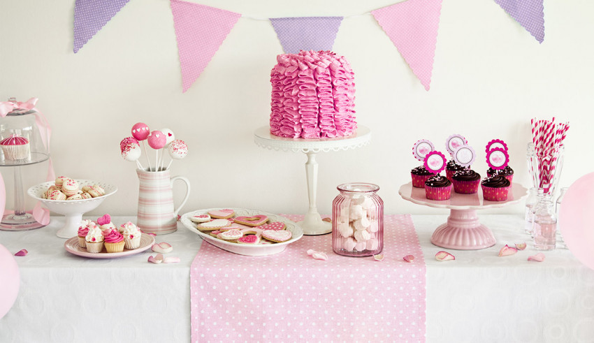 A pink and white dessert table with cupcakes and cookies.
