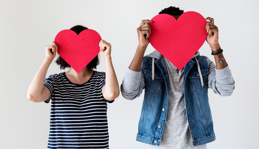 Two people holding red hearts in front of their faces.