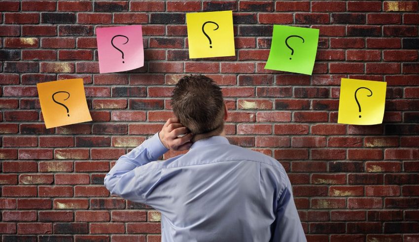 Businessman looking at question marks on a brick wall.