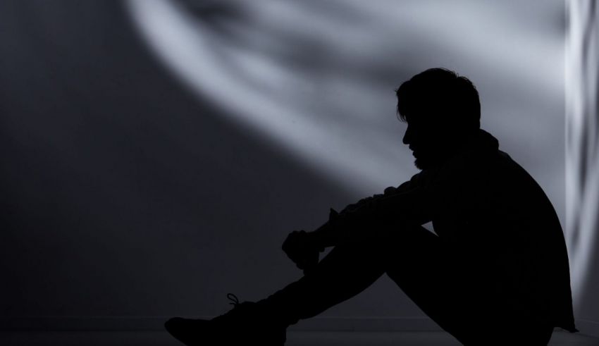 A silhouette of a man sitting on the floor in a dark room.