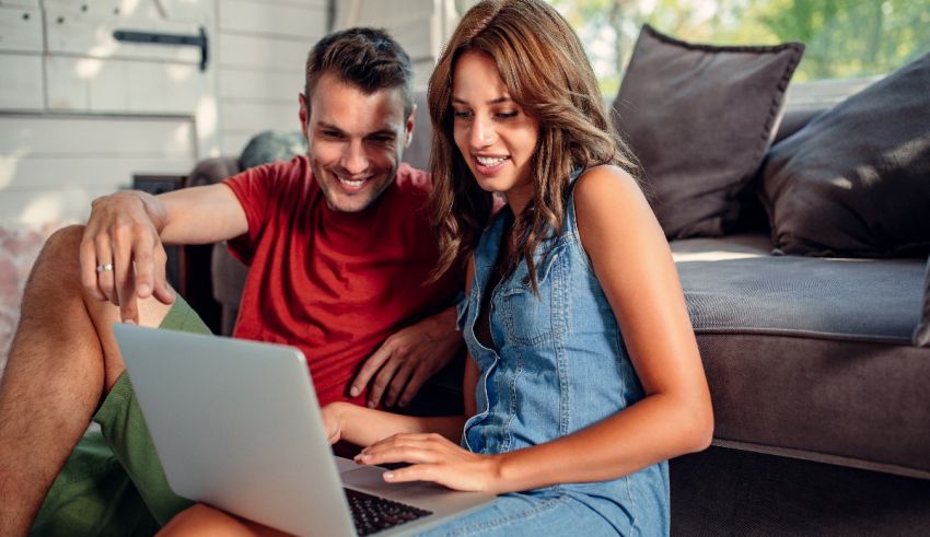 A man and woman sitting on a couch using a laptop.