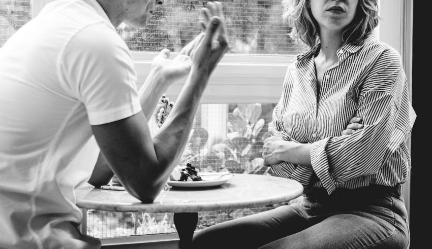 Black and white photo of a man and woman talking at a table.