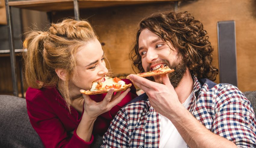 A man and woman eating pizza on a couch.