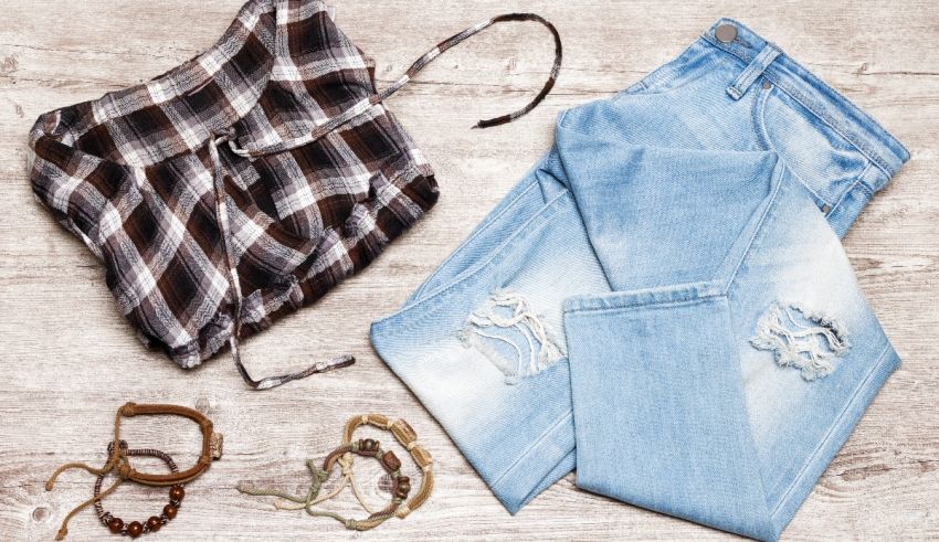 A plaid shirt, jeans and bracelets are laid out on a wooden table.