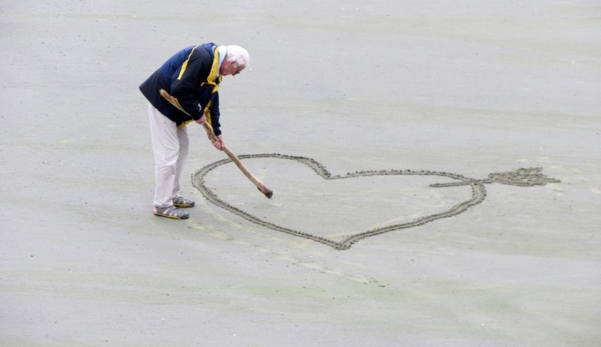 A man is drawing a heart in the sand.