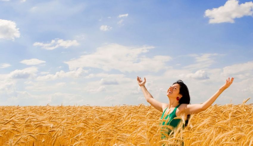 A woman standing in a wheat field with her arms outstretched.