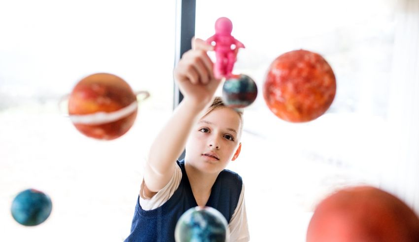 A young boy playing with paper planets in front of a window.