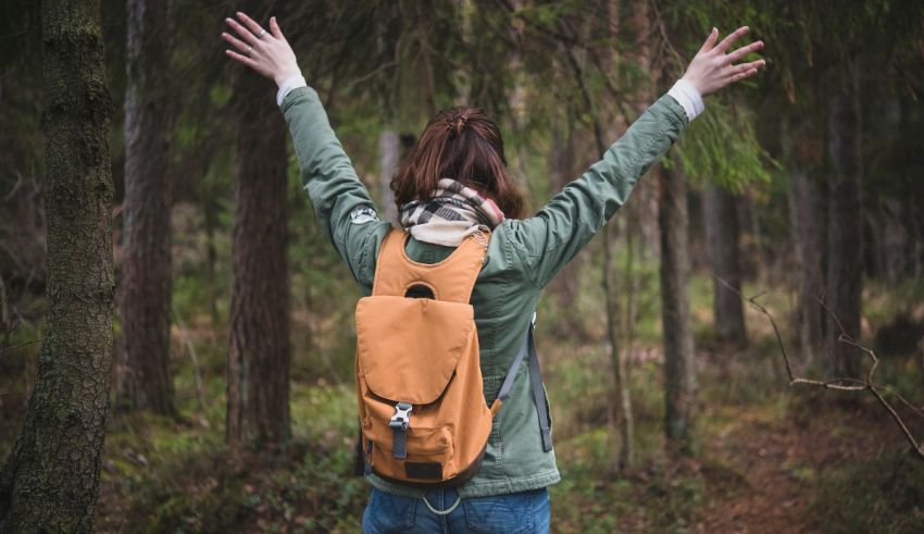 A woman with a backpack in the woods with her arms outstretched.