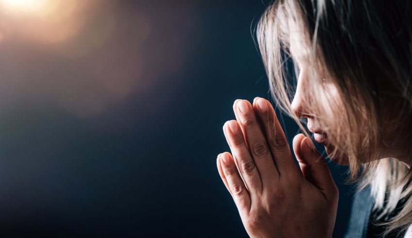 A young woman praying in front of a dark background.