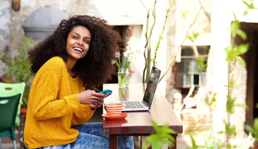 A young woman with curly hair sitting at a table with a laptop and a cup of coffee.