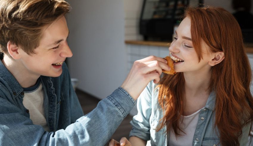 A young man and woman sharing a donut in a cafe.