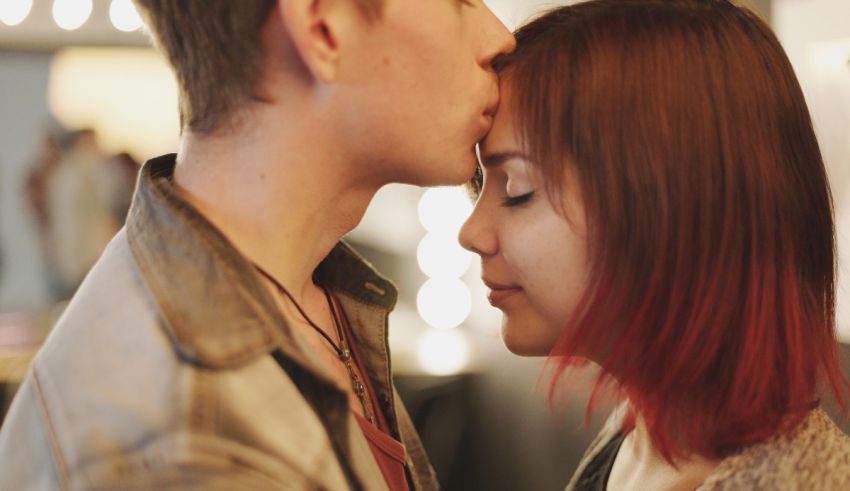 A young man and woman kissing in front of a mirror.