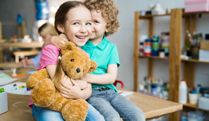 Two children sitting on a table holding a teddy bear.