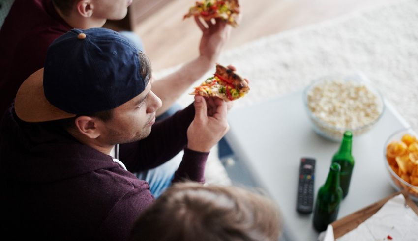 A group of people eating pizza while watching tv.