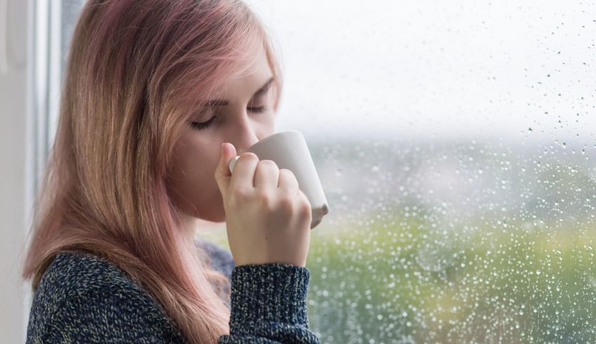 A girl drinking a cup of coffee while looking out a window.