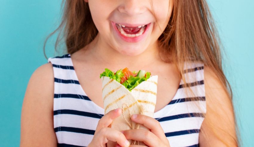 A girl is eating a wrap with a smile on her face.