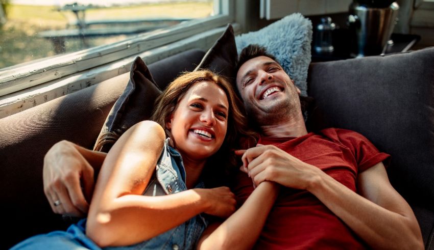 A man and woman are smiling while sitting on a couch.