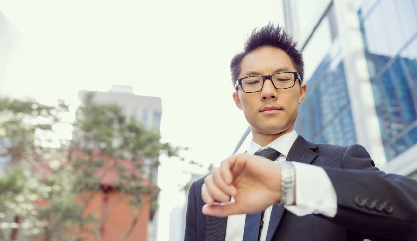 A businessman wearing glasses and a suit is looking at his watch.