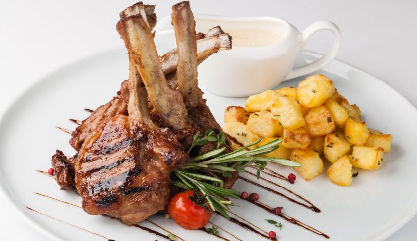 A plate with lamb chops and potatoes on it.