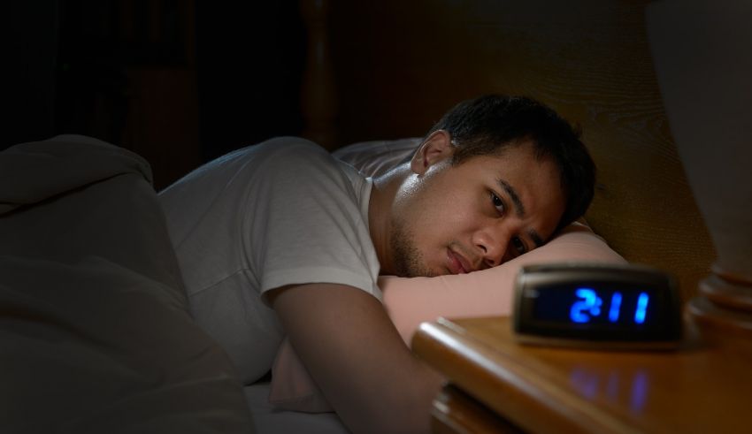 A man laying in bed with an alarm clock.