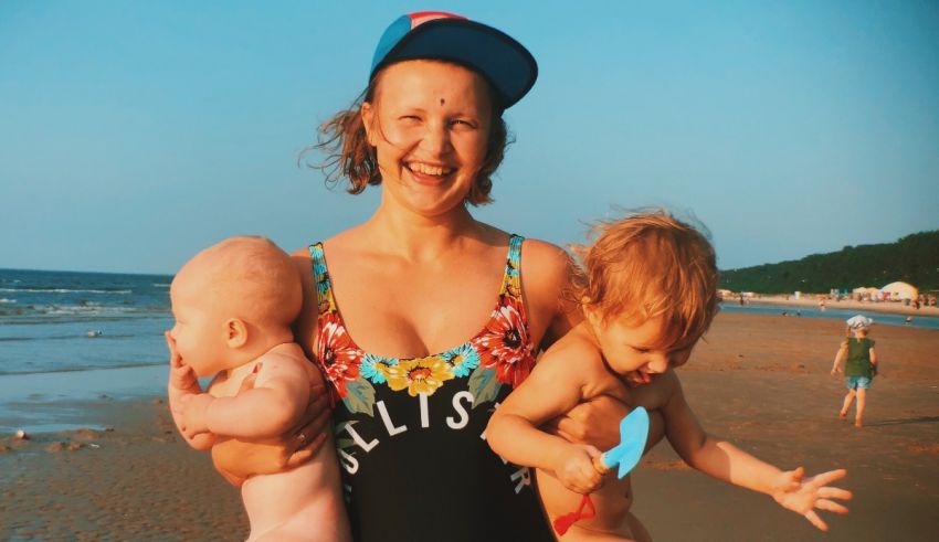A woman holding two babies on the beach.