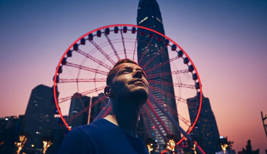 A man standing in front of a ferris wheel at dusk.