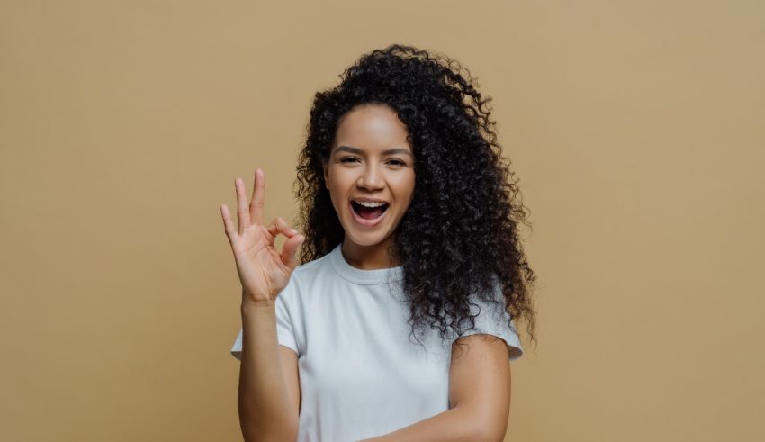 A young afro-american woman showing the ok sign on a beige background.