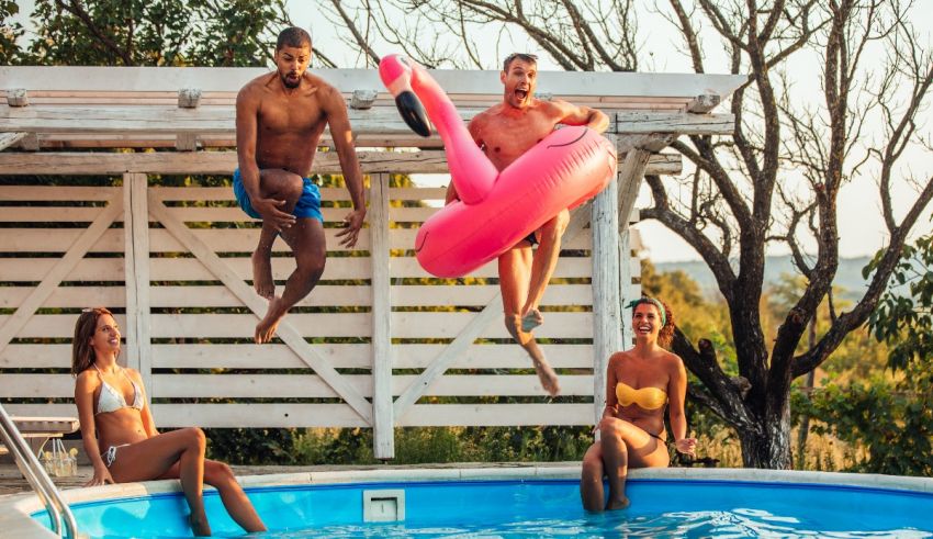 A group of people jumping into a pool with a flamingo float.