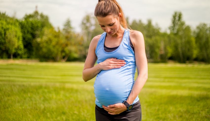 A pregnant woman is holding her stomach in a field.