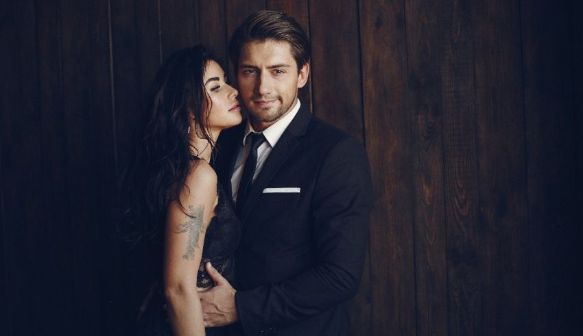 A man and woman posing in front of a wooden wall.