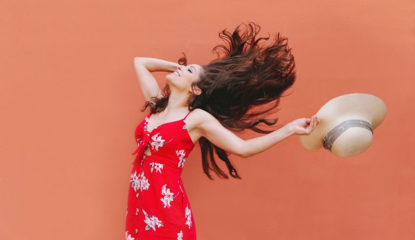 A woman in a red dress and hat with her hair blowing in the wind.