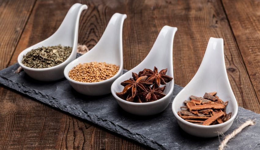 Four spoons with different spices on a slate.