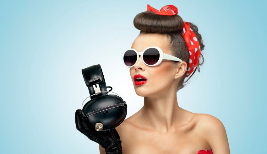 A woman wearing sunglasses and a red bandana holding a pair of headphones.