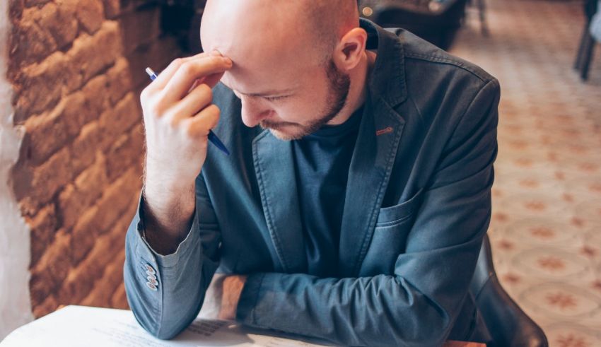 A bald man sitting at a table with his head in his hands.